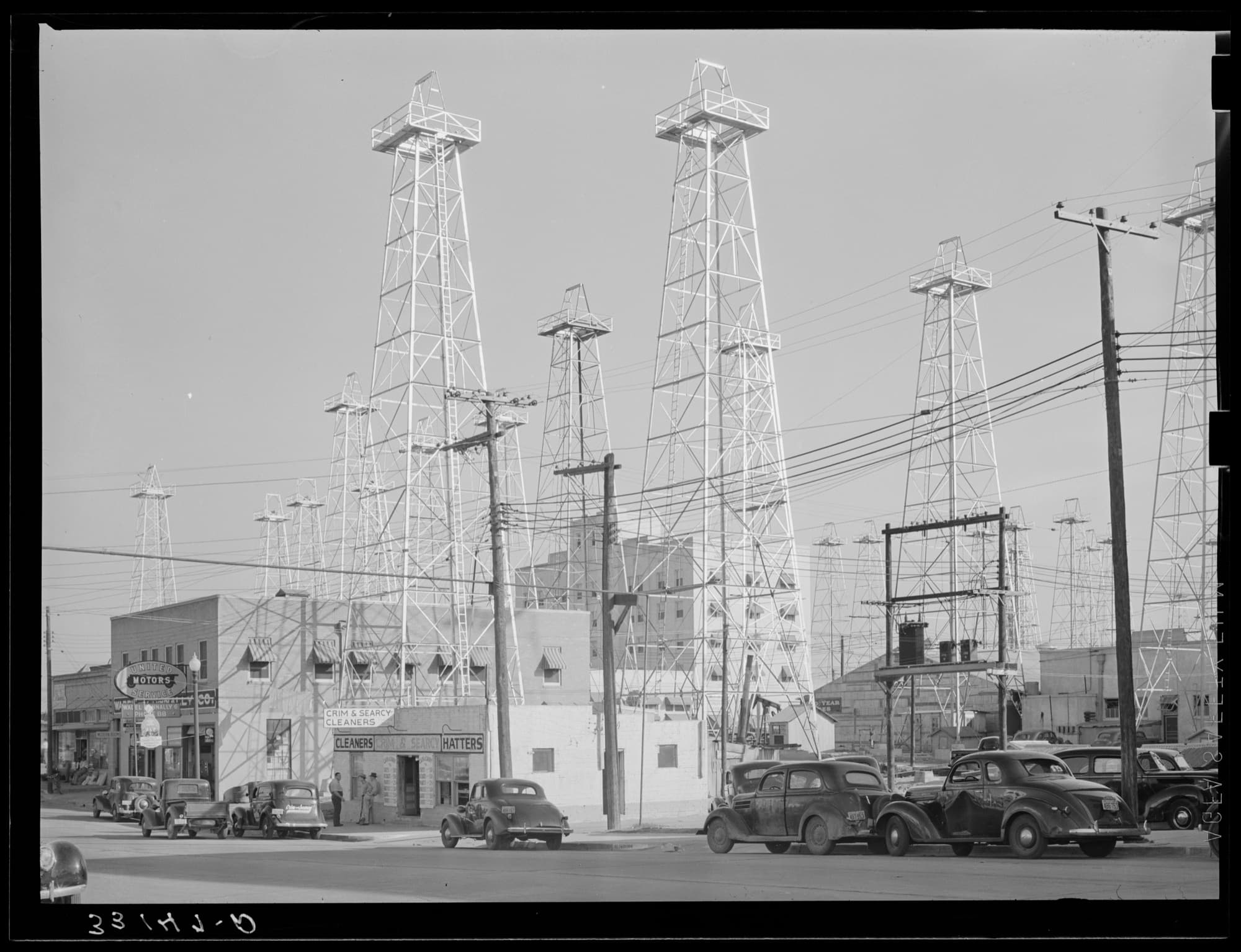 Oil derricks towering over downtown Kilgore, Texas in 1939, storefronts and parked cars beneath them
